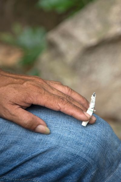 A man is smoking Cigarette and is wearing jeans