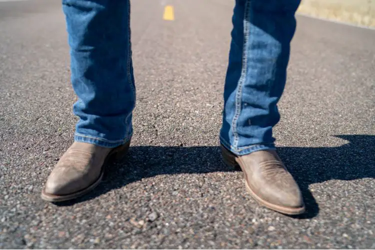 A man wears jeans and cowboy boots and is standing on the road