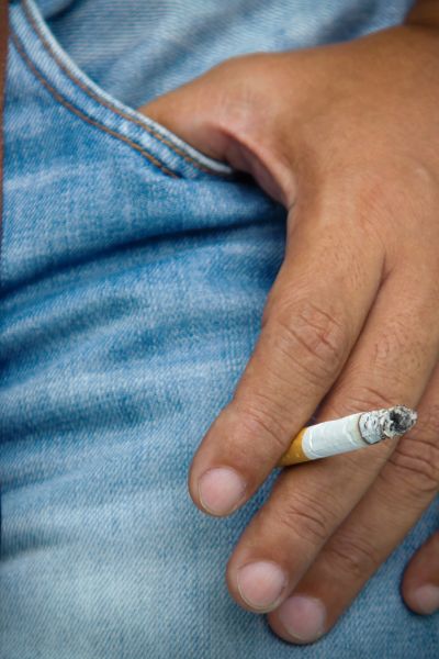 A man wears jeans and is smoking cigarette