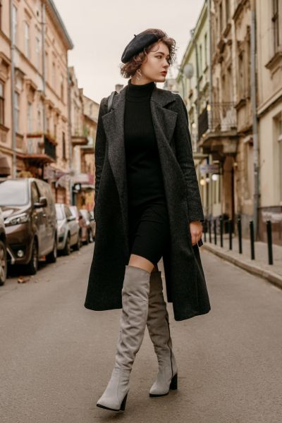 A woman wears grey over the knee cowboy boots with beret and blazer