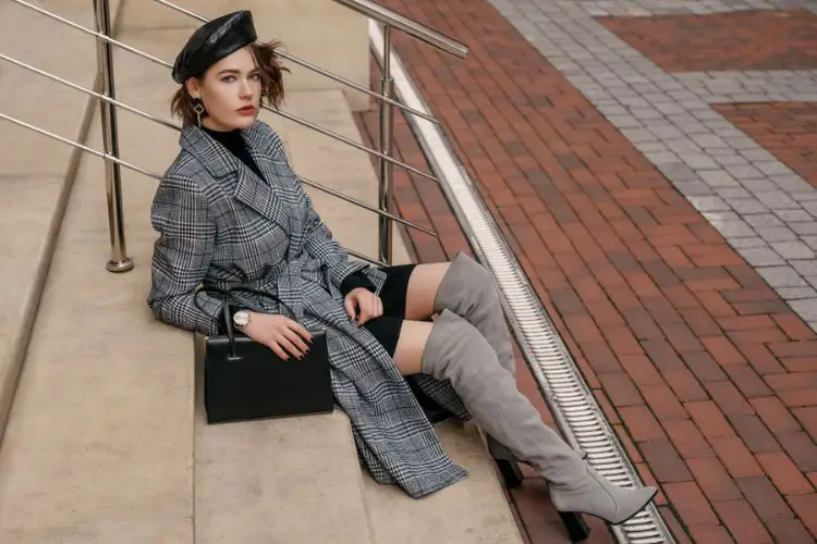 A woman wears grey over the knee cowboy boots with grey plaid blazer