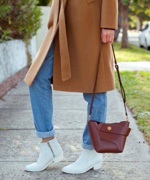 A woman wears loose fit jeans with white cowboy boots and brown blazer