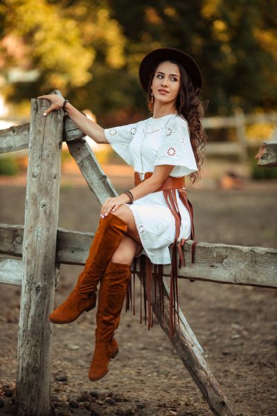 A woman wears over the knee boots with white dress on the ranch