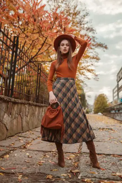 A woman wears skirts with long sleeves turtleneck and over the knee cowboy boots.