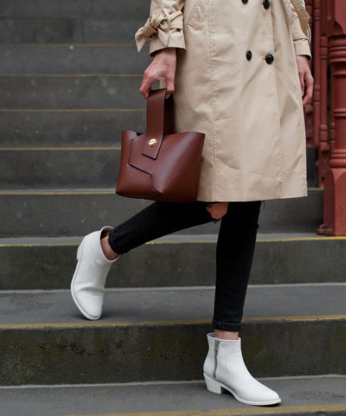 A woman wears white ankle cowboy boots with black jeans and brown leather bag