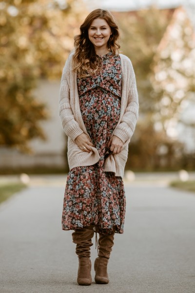 A woman wears boho dress, cardigan and cowboy boots and is standing on the road
