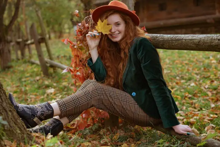 A woman wears cowboy boots, pants, wool coat in fall