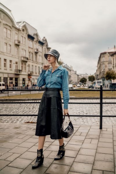 A woman wears skirt with ankle cowboy boots and denim shirt