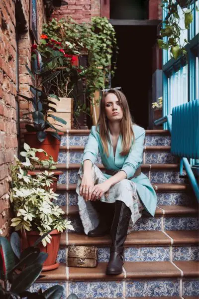 A woman wears dresses and cowboy boots and is sitting on the stairs