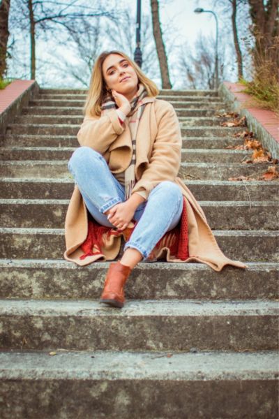 A woman wears jeans, cowboy boots and blazer and are sitting on the stairs
