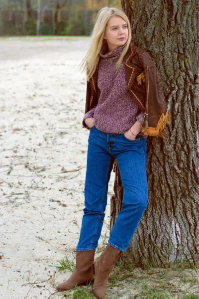 A woman wears jeans with leather jacket and a sweater