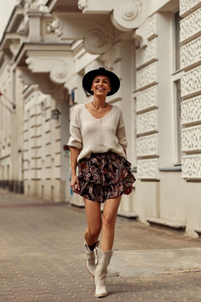 A woman wears short skirt with sweater and short cowboy boots for casual outings
