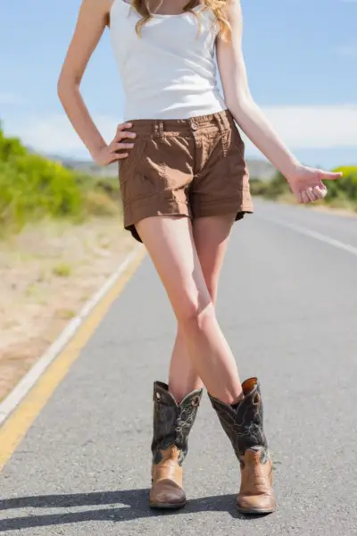 A woman wears shorts with brown cowboy boots on the street