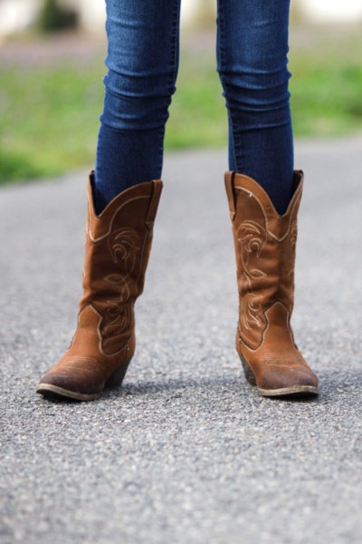A woman wears skinny jeans and brown cowboy boots