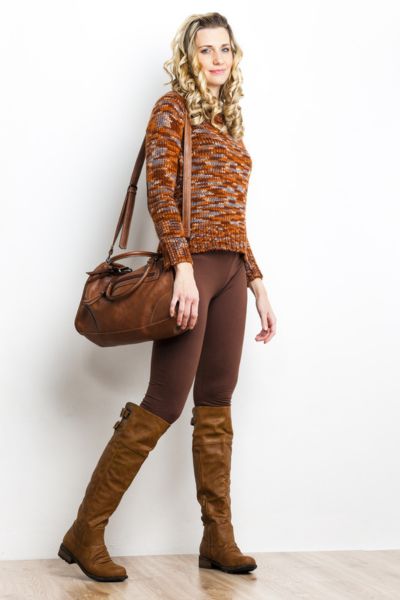 A woman wears skinny pants, sweater, leather bag and cowboy boots