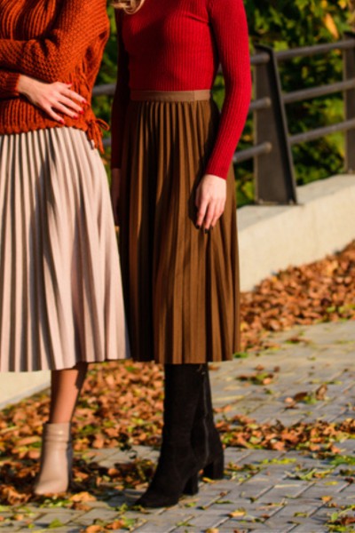 A woman wear sweater, belt, pleated skirt and cowboy boots