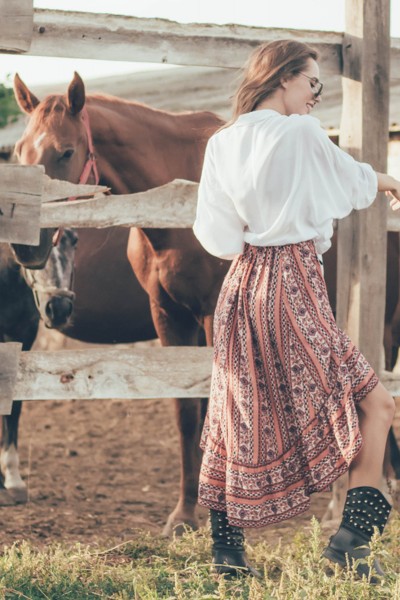 A woman wears a pleated skirt with black cowboy boots on the ranch
