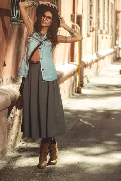 A woman wears a pleated skirt with cowboy boots and denim jacket