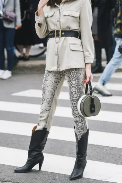 A woman wears black cowboy boots with belt and blazer