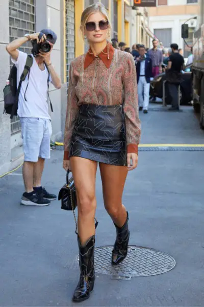 A woman wears black leather skirt with black cowboy boots