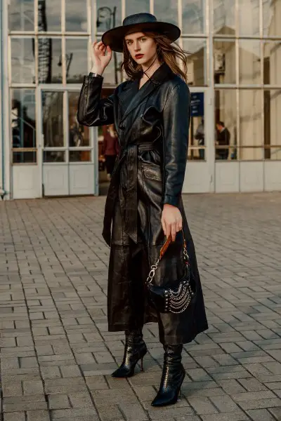 A woman wears black trench coat with black cowboy boots and black hat