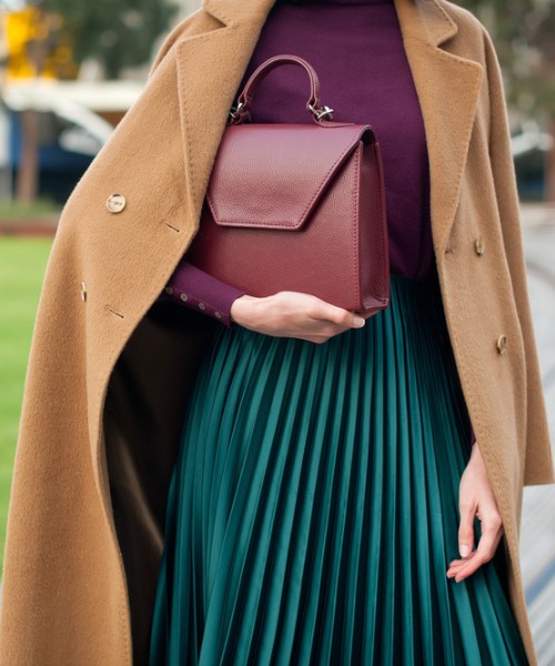 A woman wears blazer, pleated skirt and holding a leather handbag