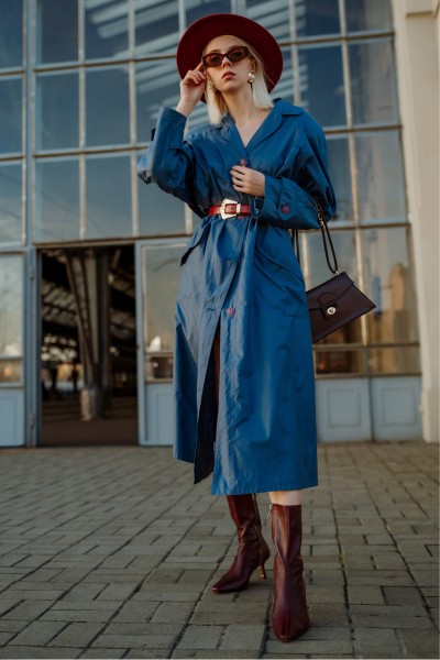 A woman wears blue trench coat with cowboy boots, tote and hat