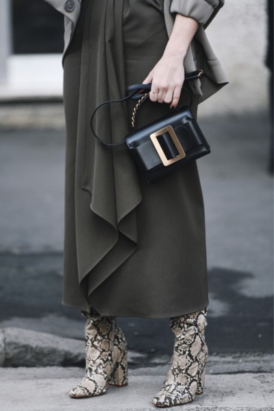 A woman wears snakeskin cowboy boots with black dress and are holding a black bag