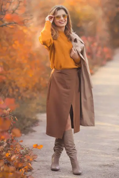 A woman wears trench coat, sweater and cowboy boots
