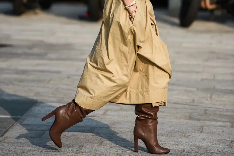 A woman wears trench coat with brown leather cowboy boots