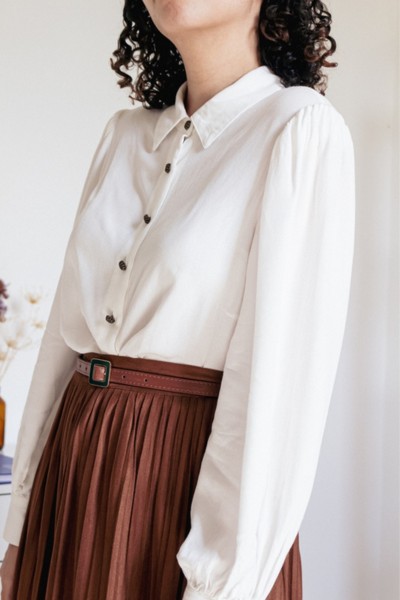 A woman wears white blouse with a brown pleated skirt