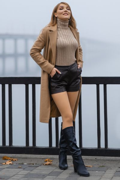 A woman wears black cowboy boots with skirt, sweater and blazer