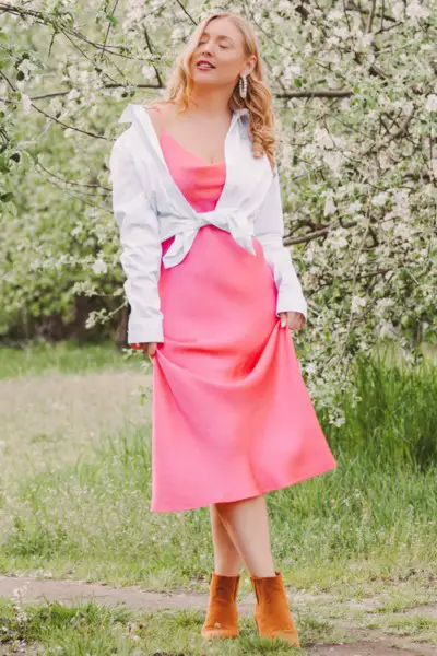 A woman wears blouse over pink dress and ankle cowboy boots