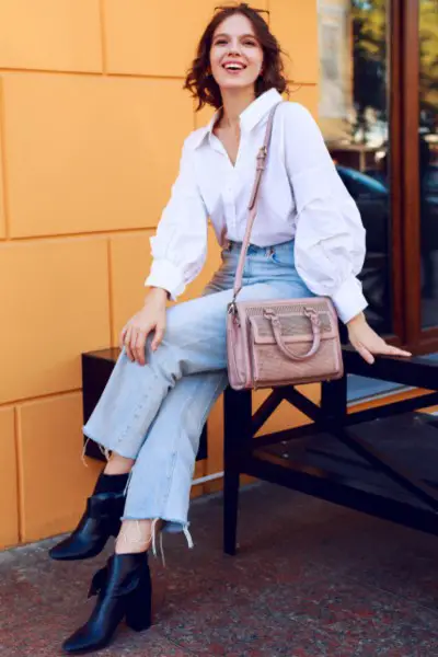 A woman wears blouse with ripped hem jeans and black cowboy boots and crossoverbag