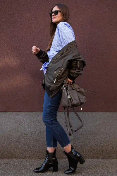 A woman wears blue jeans with black ankle boots, bomber coat and blouse