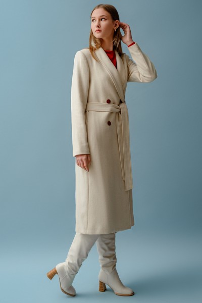 A woman wears cream trench coat with white cowboy boots