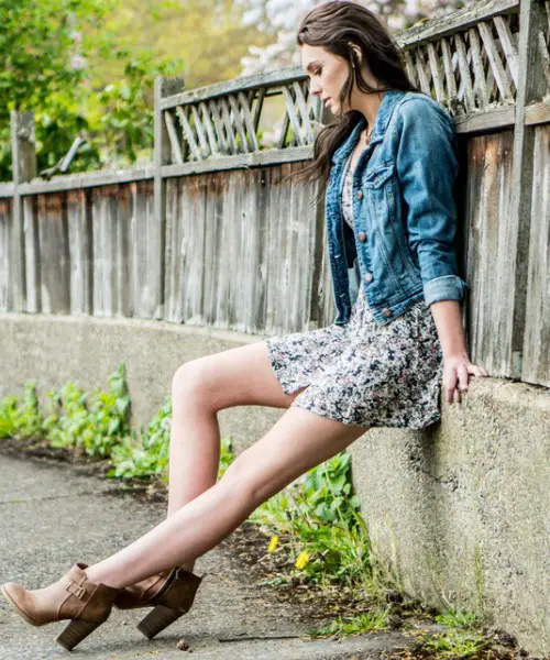 A woman wears denim jacket with dress and cowboy boots