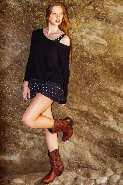 A woman wears dotted black skirt with black top and ankle cowboy boots