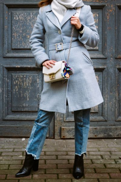 A woman wears frayed jeans with black cowboy boots and trench coat