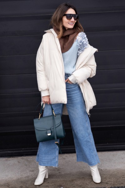 A woman wears coat with sweater, wide leg jeans and white cowboy boots