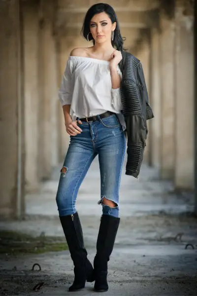 A woman wears jeans, black cowboy boots, off shoulder t shirt and a coat