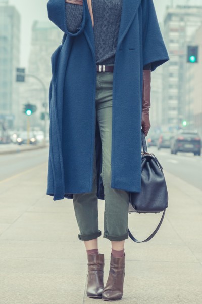 A woman wears jeans with ankle boots, trench coat and handbag