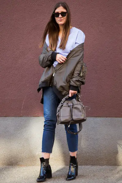 A woman wears jeans with black ankle boots, bomber jacket and blouse