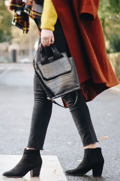 A woman wears jeans with black cowboy boots, sweater and red coat