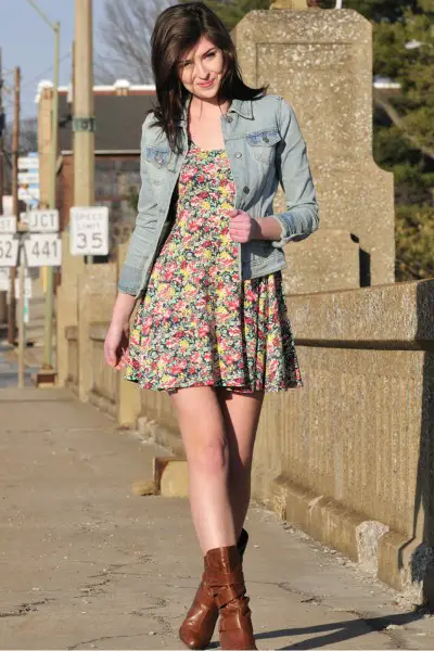 A woman wears short floral dress with ankle cowboy boots and denim jacket