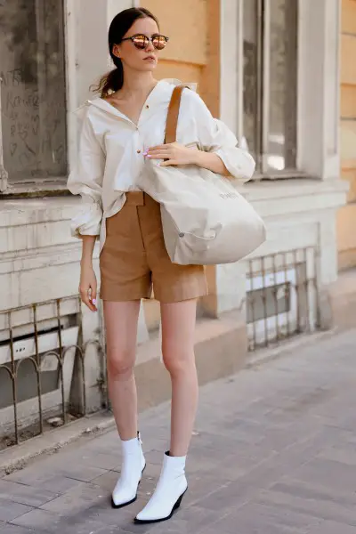 A woman wears shorts with blouse and white ankle boots