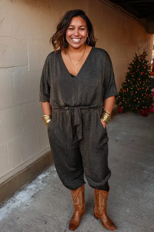 A plus-size woman wears brown cowboy boots with a glittery black jumpsuit and gold bangles at a casual winter party