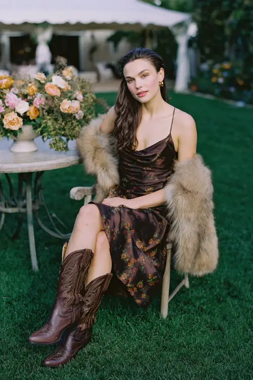 A woman styles brown cowboy boots with a dark floral satin slip dress and a soft faux fur stole