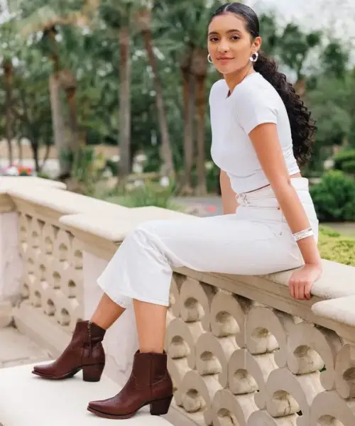 A woman wears The Daisy Boots with white outfit and is sitting.
