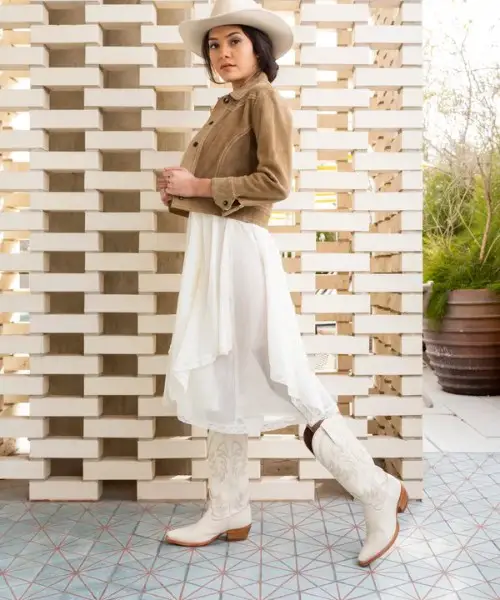 A woman wears a white skirt with white cowboy boots